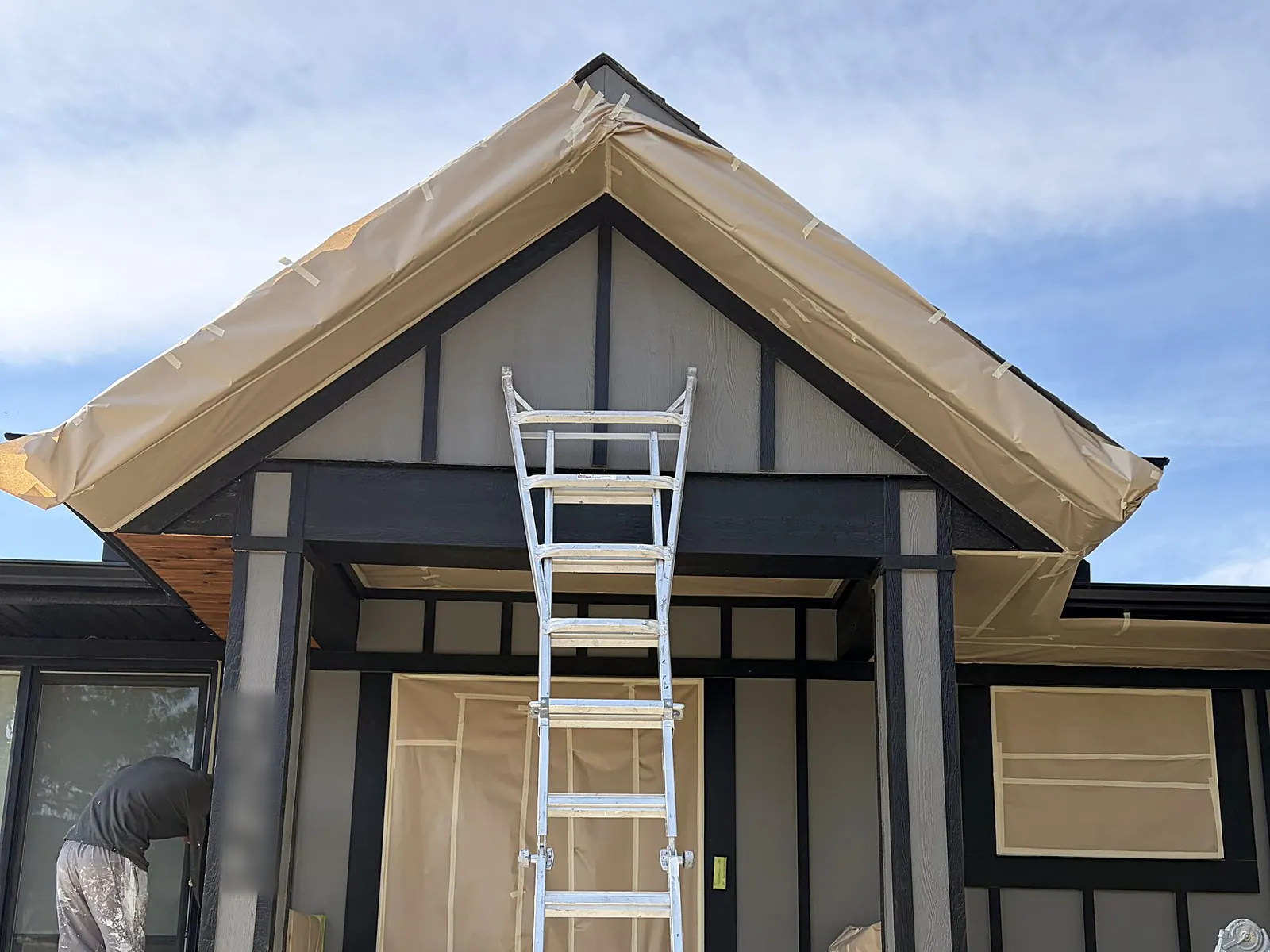 The same bungalow during prep: grey siding, windows and door masked in paper, ladders up