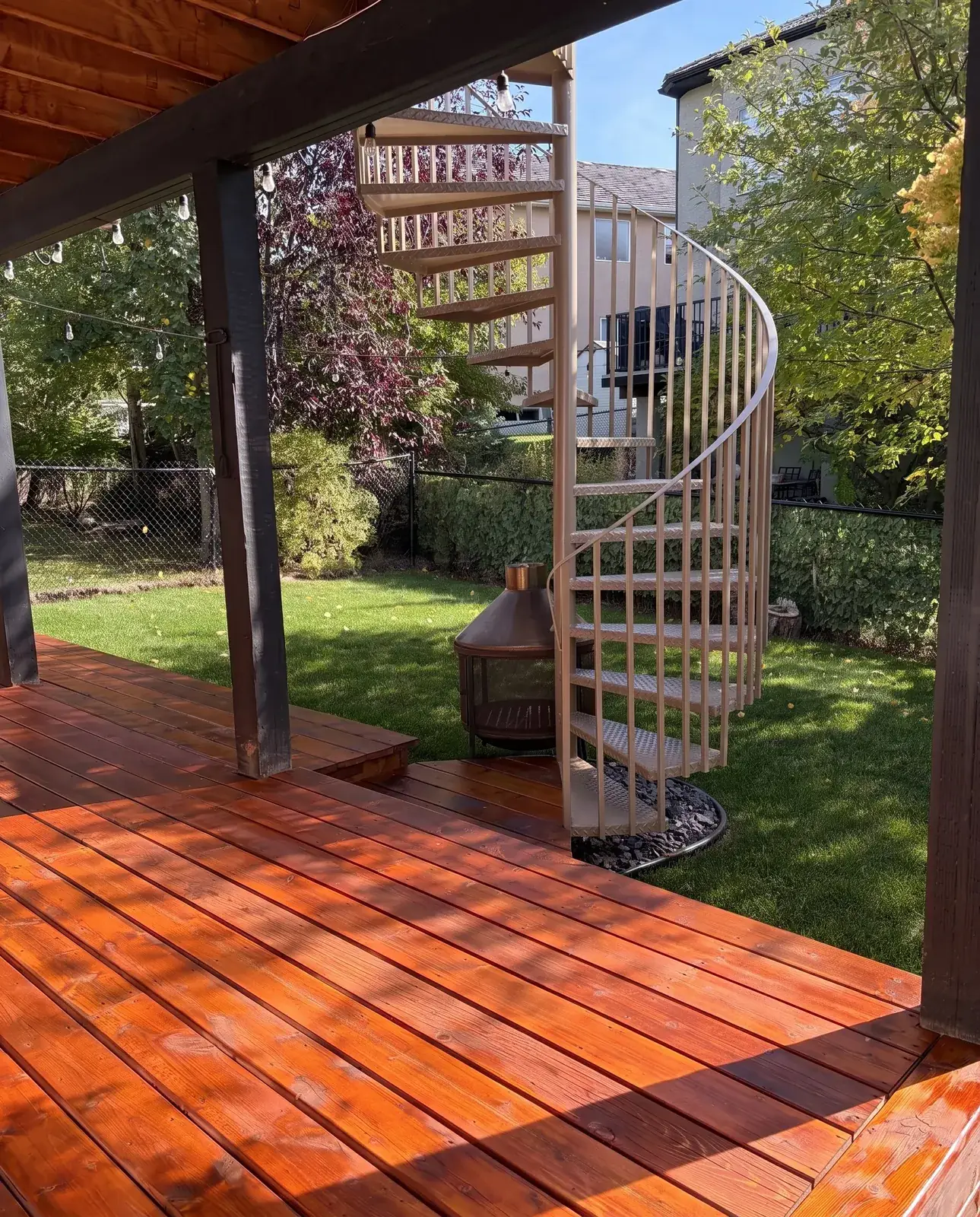 A cedar deck freshly stained a deep amber, with a spiral stair and a lawn beyond