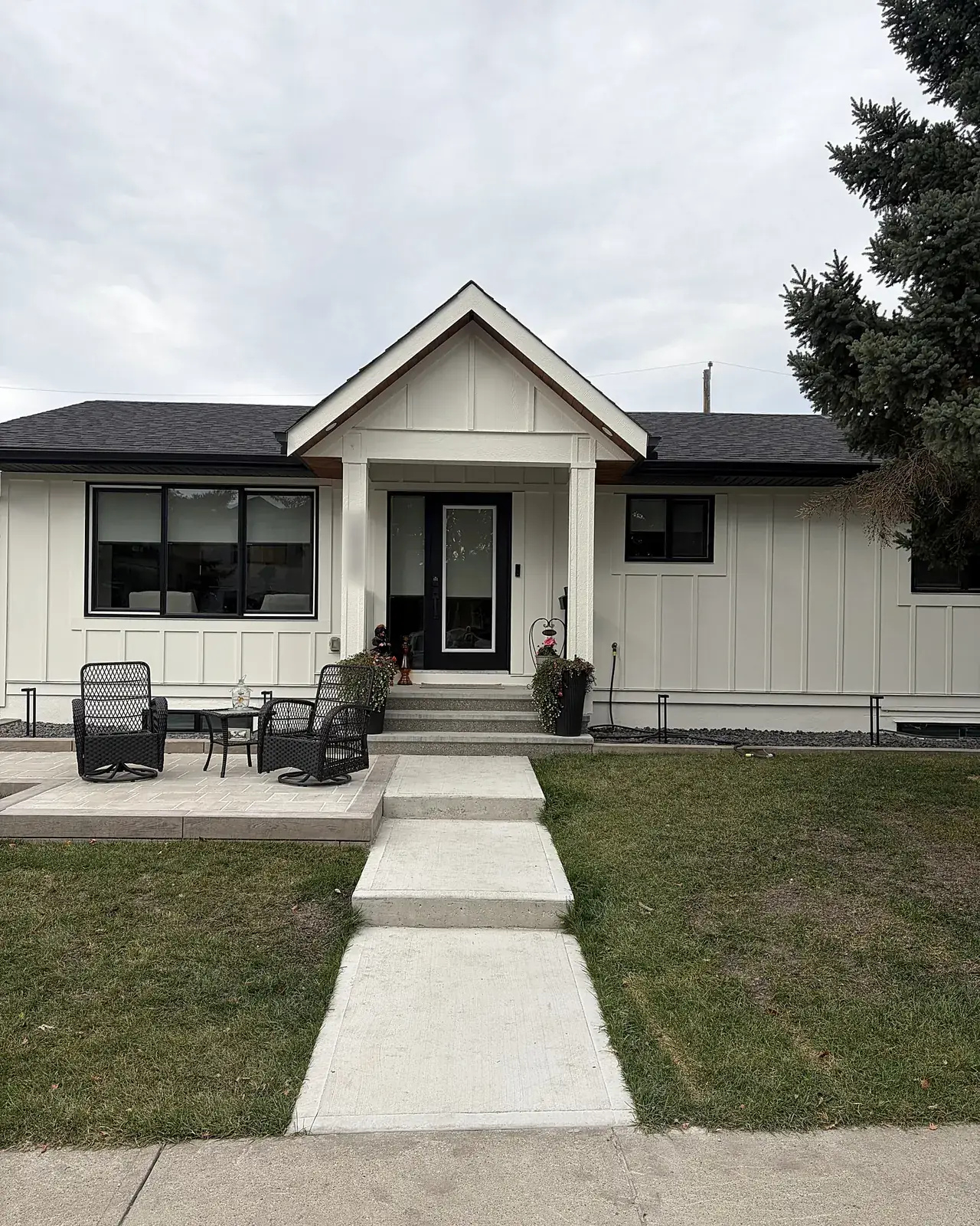 The front of a white board-and-batten bungalow with a gabled porch and black door