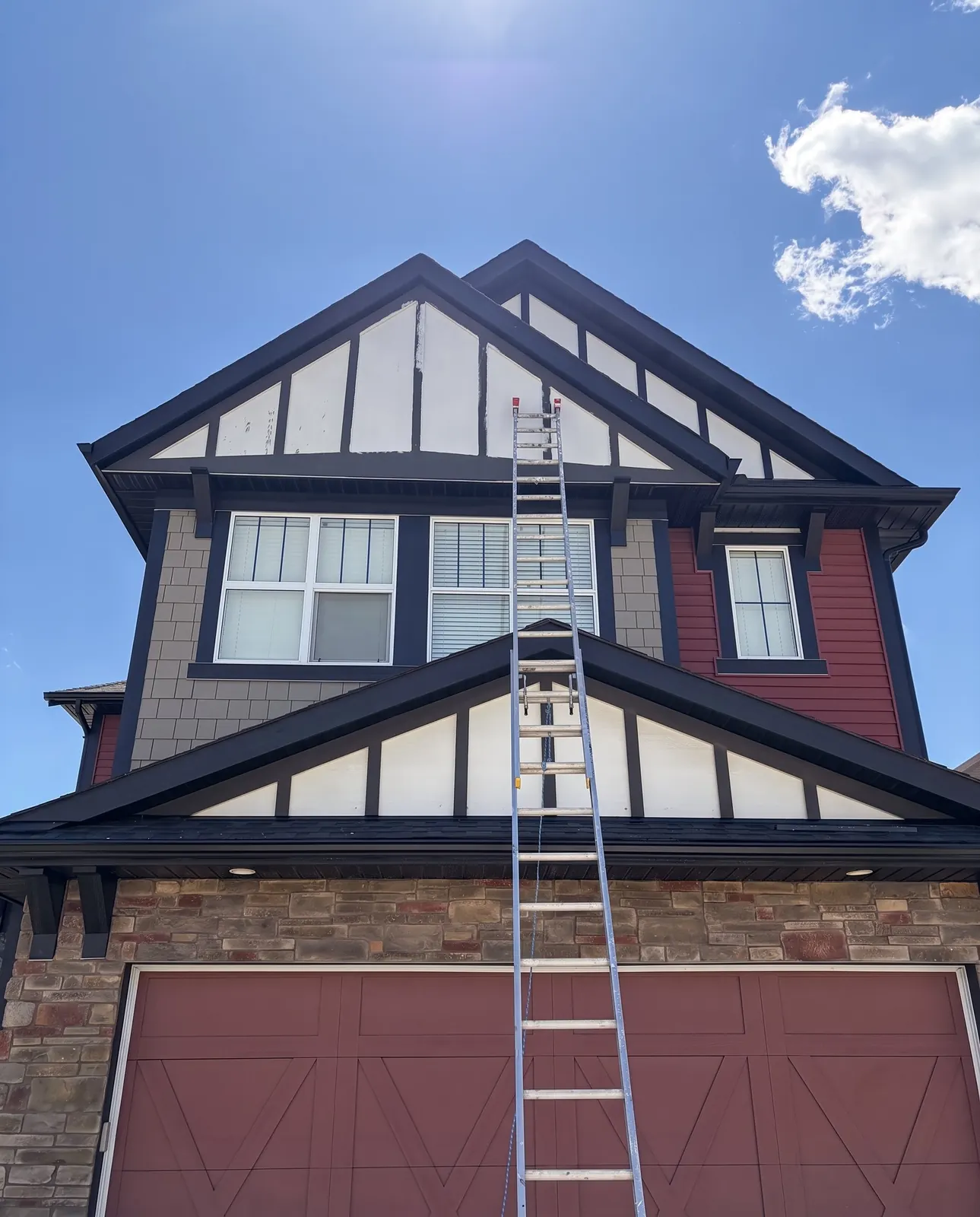 A two-storey house with red siding and dark trim, a ladder up to the gable