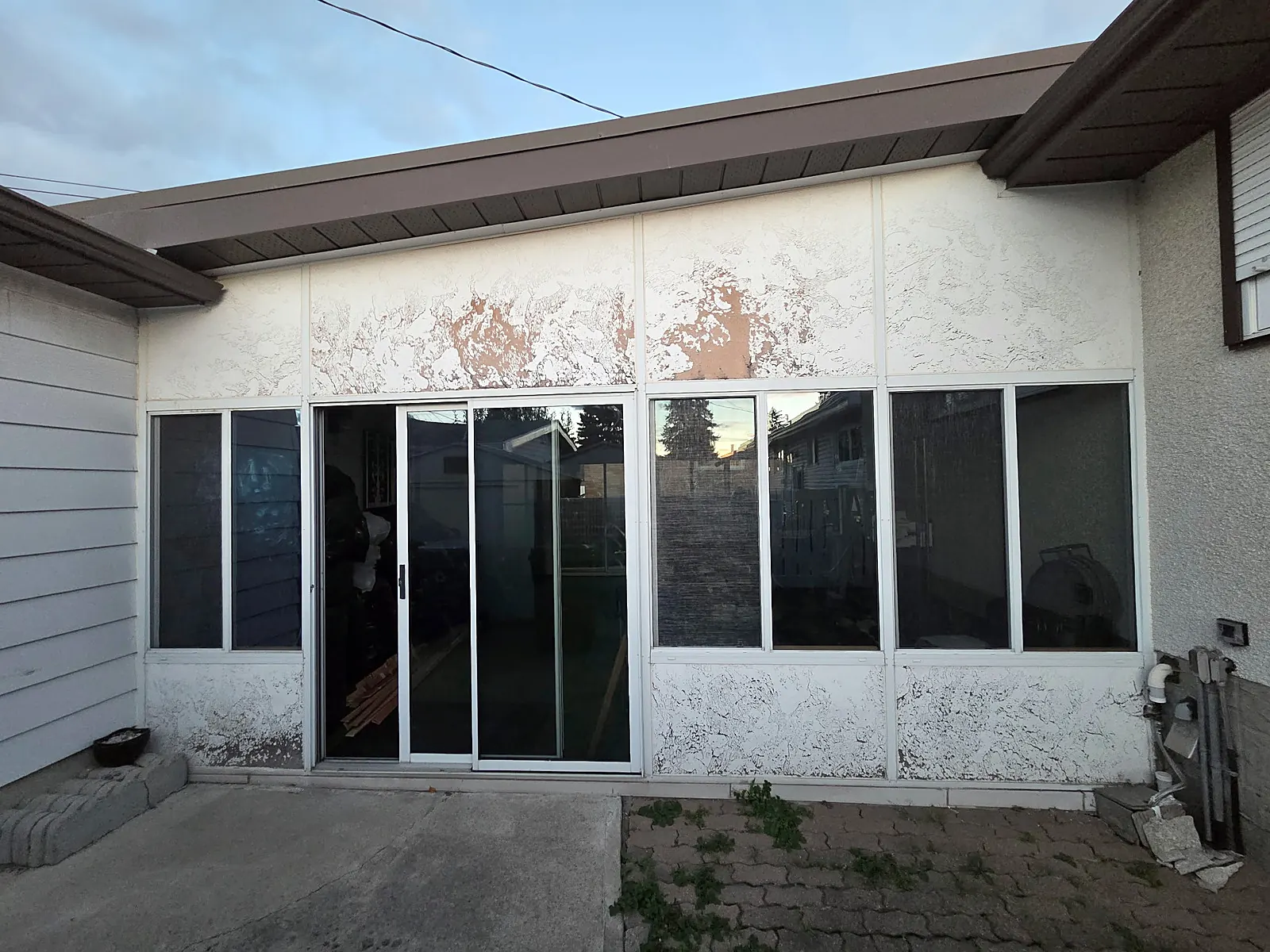 A stucco sunroom with peeling, flaking paint before work starts